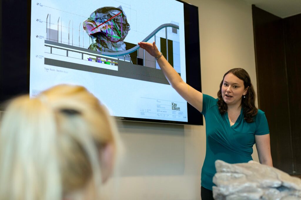 A female engineer delivers a presentation on rollercoaster design using a digital screen in an office.